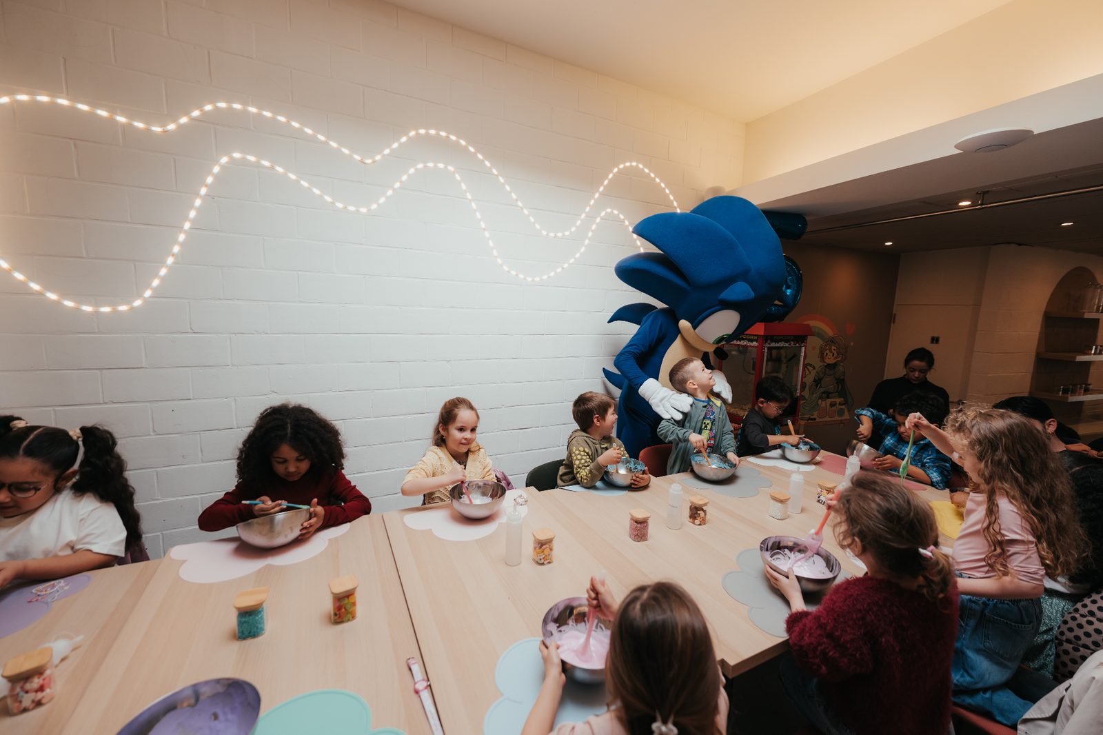 Anniversaire chez Slime Art Studio — enfants attablés en pleine création de slime avec la mascotte Sonic géante et guirlande lumineuse au mur