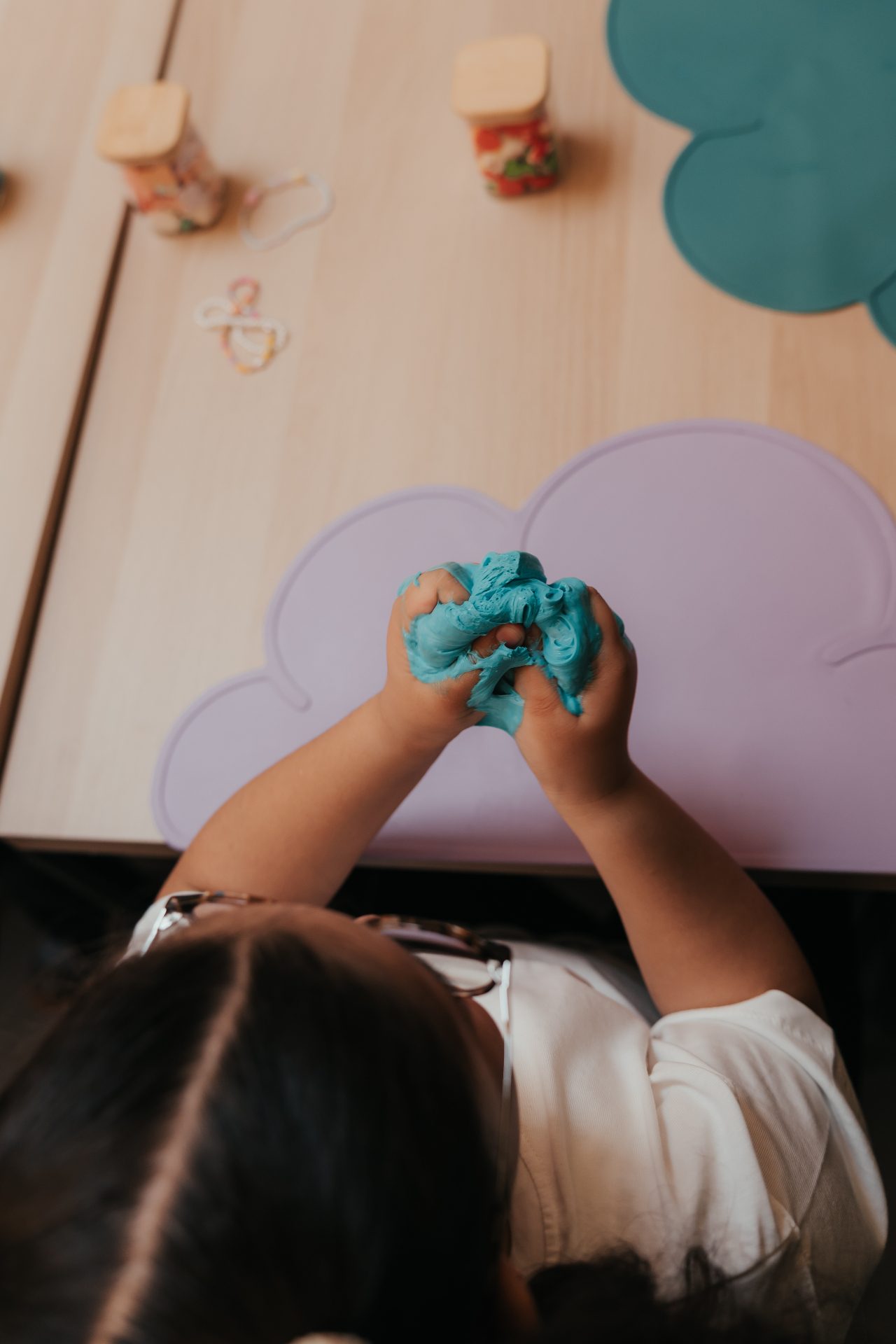 Atelier Slime Art Studio — vue plongeante sur les mains d'un enfant malaxant un slime turquoise sur un set en silicone en forme de nuage