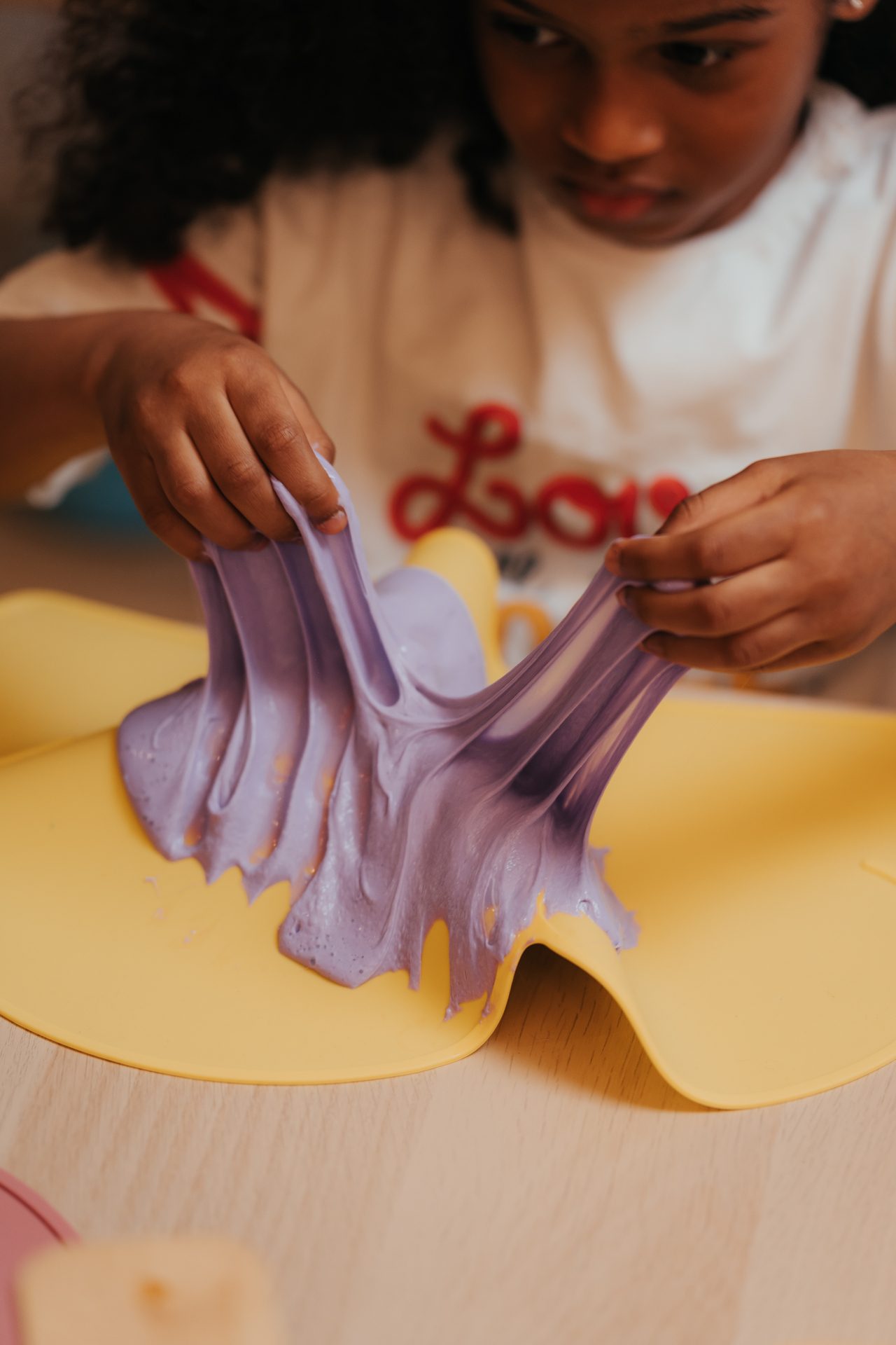 Atelier Slime Art Studio — enfant étirant un slime violet pastel dégoulinant sur un set en silicone jaune
