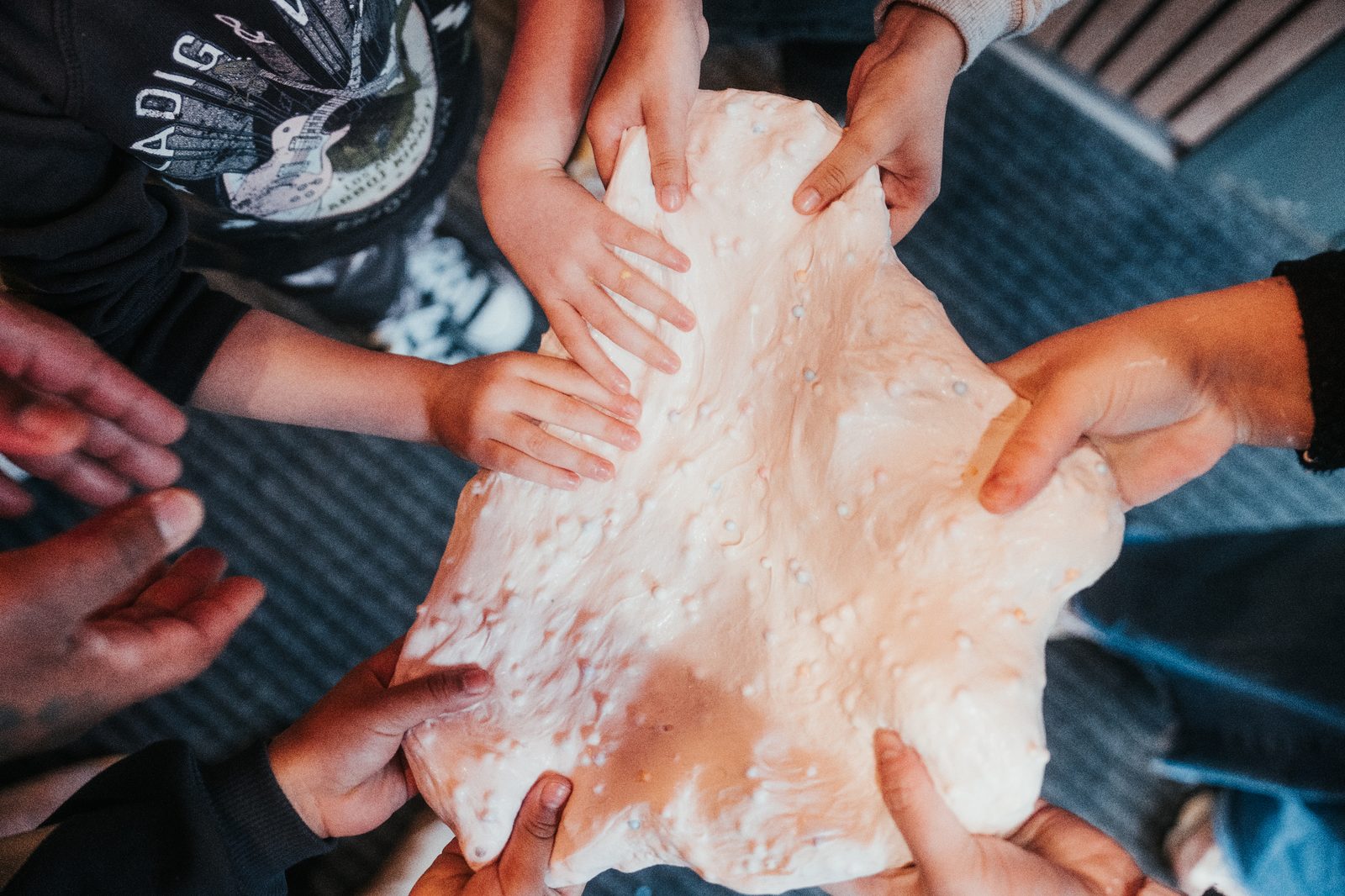 Atelier Slime Art Studio — six paires de mains d'enfants et d'adulte se rejoignant autour d'un immense slime blanc pailleté