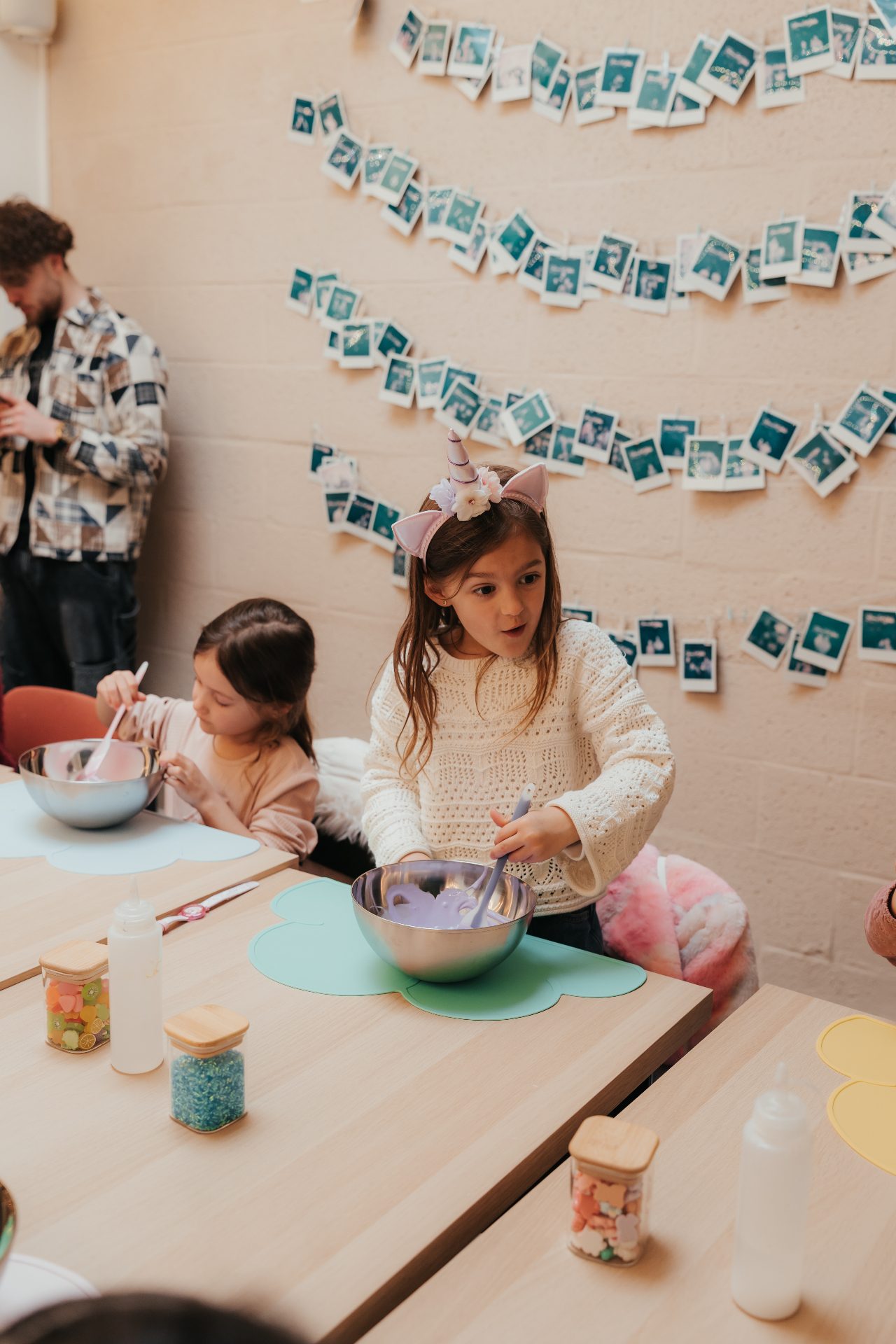 Atelier Slime Art Studio — deux enfants en pleine création de slime violet à table, devant un mur décoré de photos souvenirs