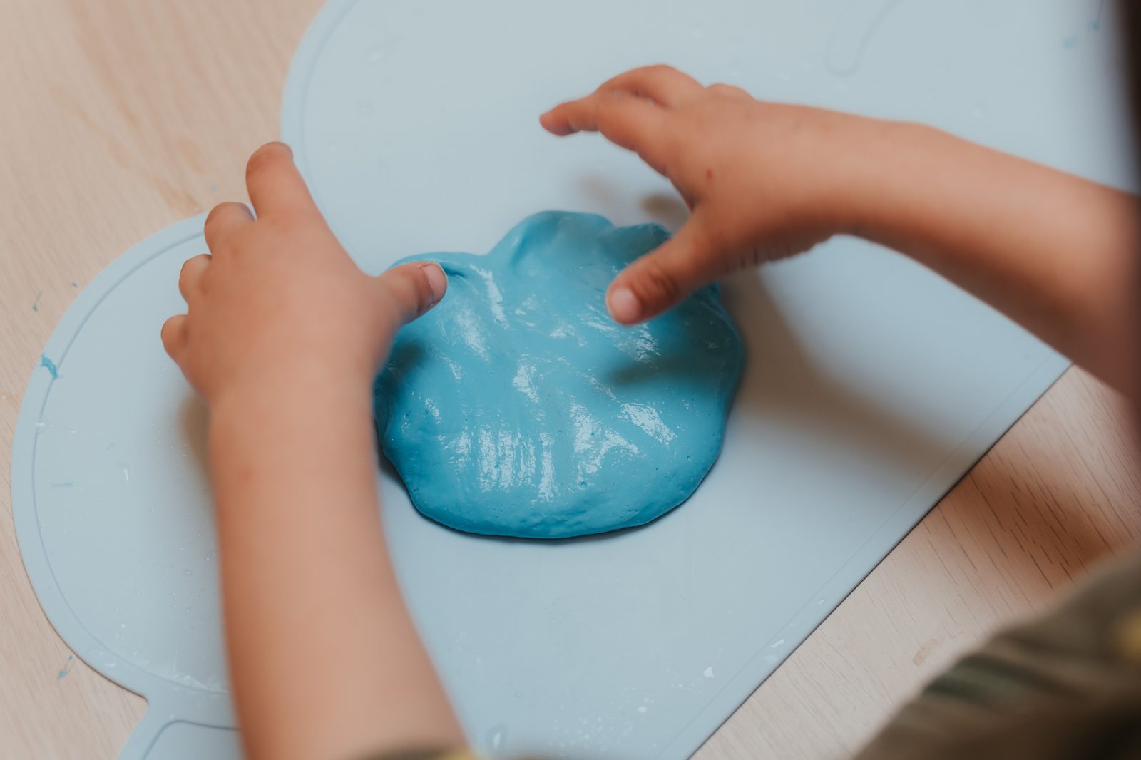Atelier Slime Art Studio — mains d'enfant appuyant sur une slime bleue brillante posée sur un set en silicone bleu clair