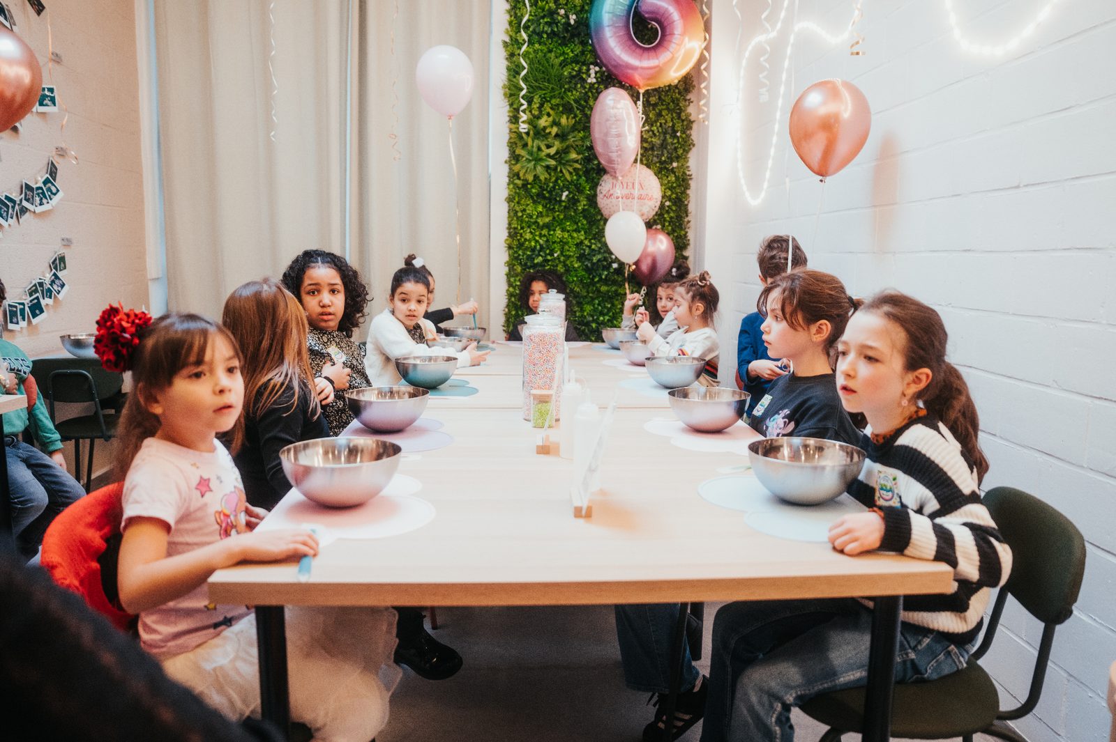 Atelier slime à Mons — enfants attablés avec bols en inox devant un mur végétal et ballons d'anniversaire
