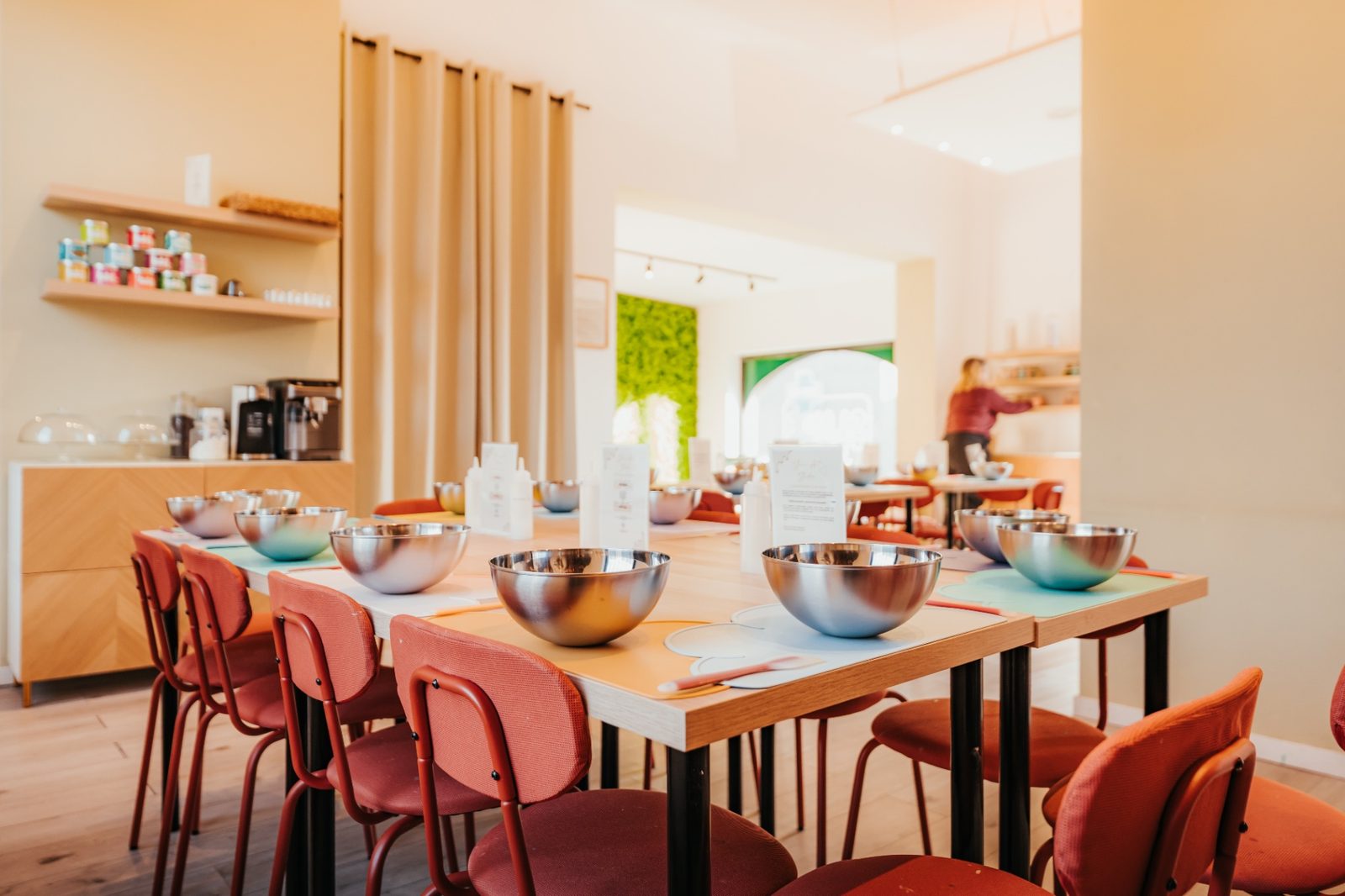 Atelier slime à Waterloo — tables en bois clair avec bols en inox, sets pastel et mur végétal en arrière-plan